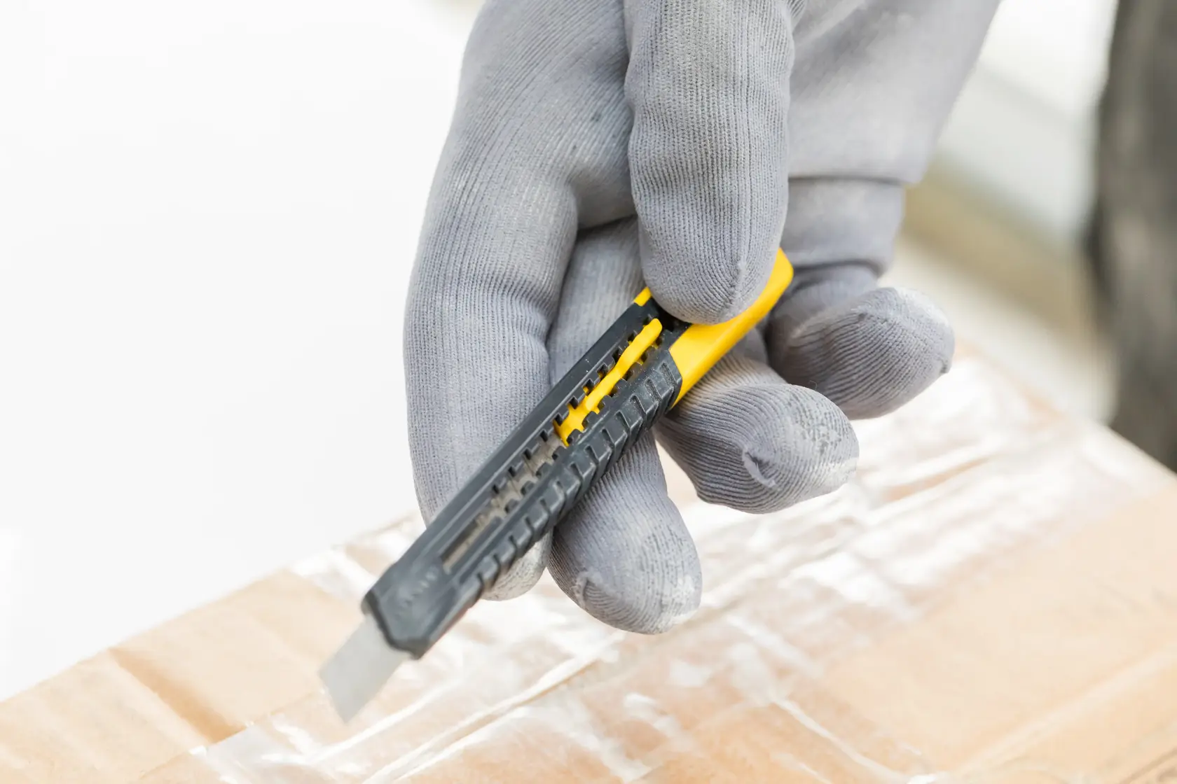 STANLEY 0-10-150 Universalmesser mit grauen Handschuhen schneidet Klebeband auf Karton, Nahaufnahme Fotografie.