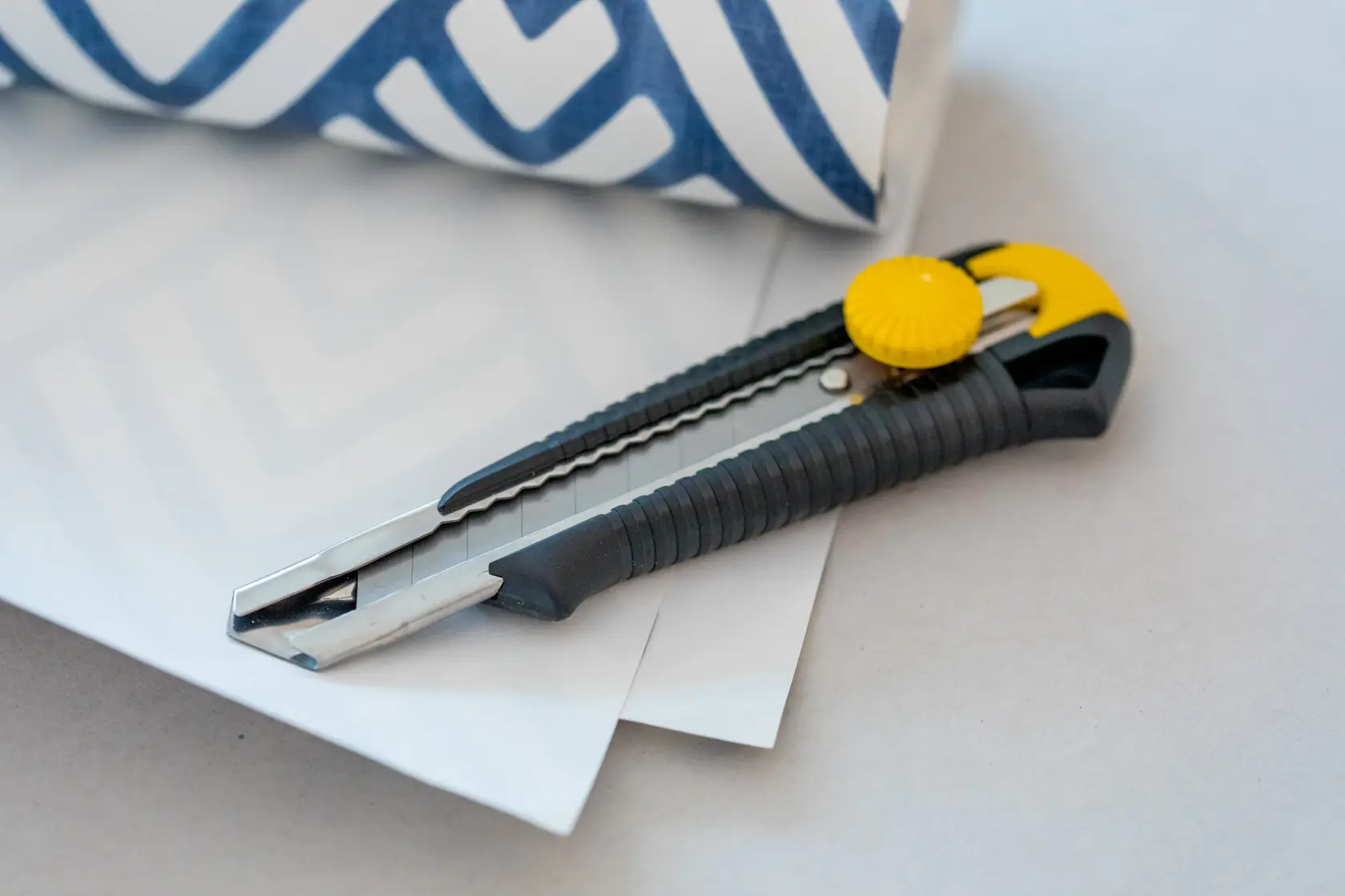 STANLEY 0-10-418 utility knife with black and yellow handle, placed on white paper next to blue patterned roll.