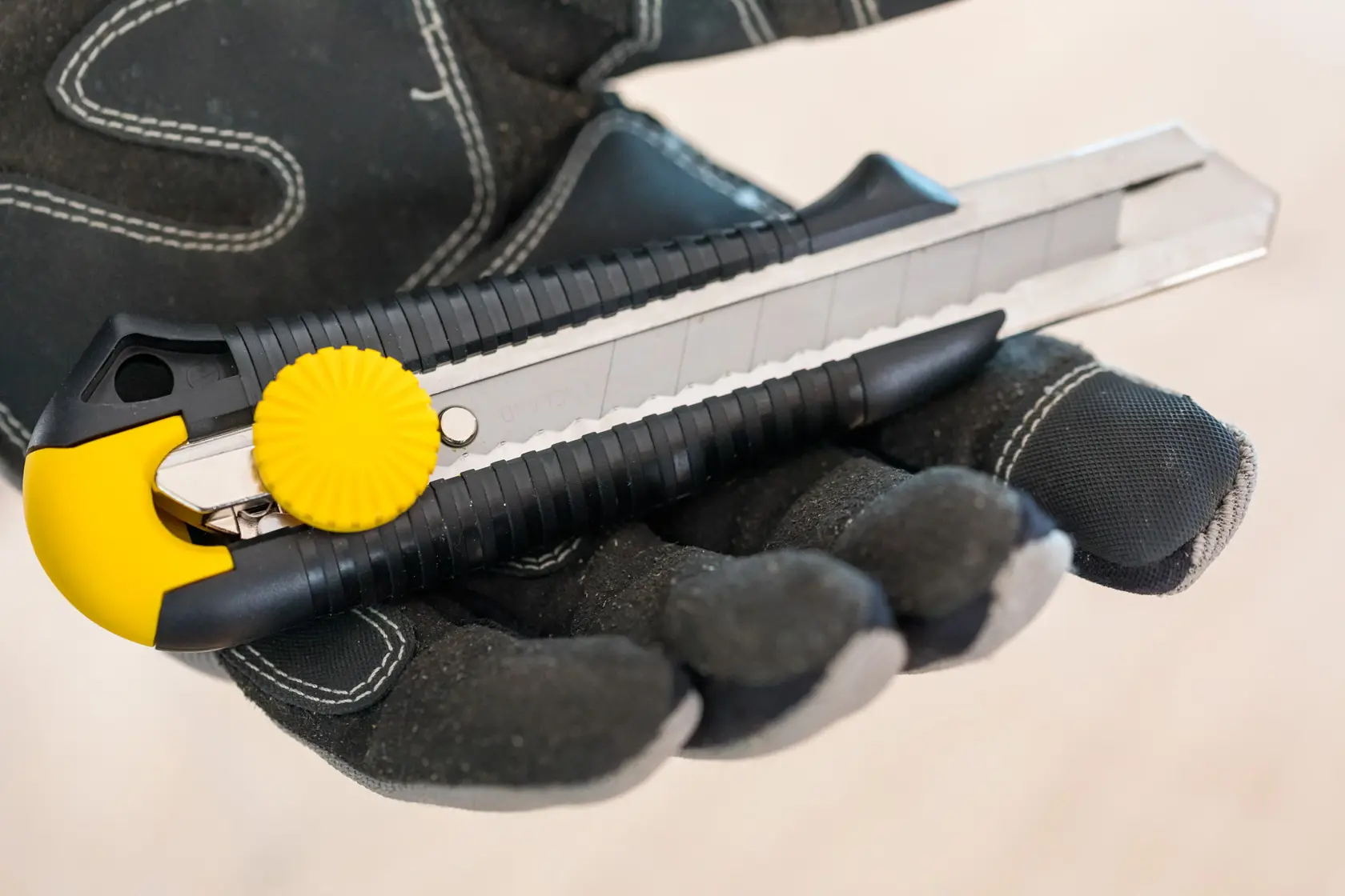STANLEY 0-10-418 utility knife with yellow lock wheel, held in black work glove, close-up photo.