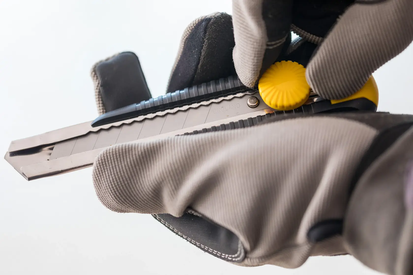 Photo of STANLEY 0-10-418 utility knife being adjusted with gloves, close-up on yellow dial and blade.