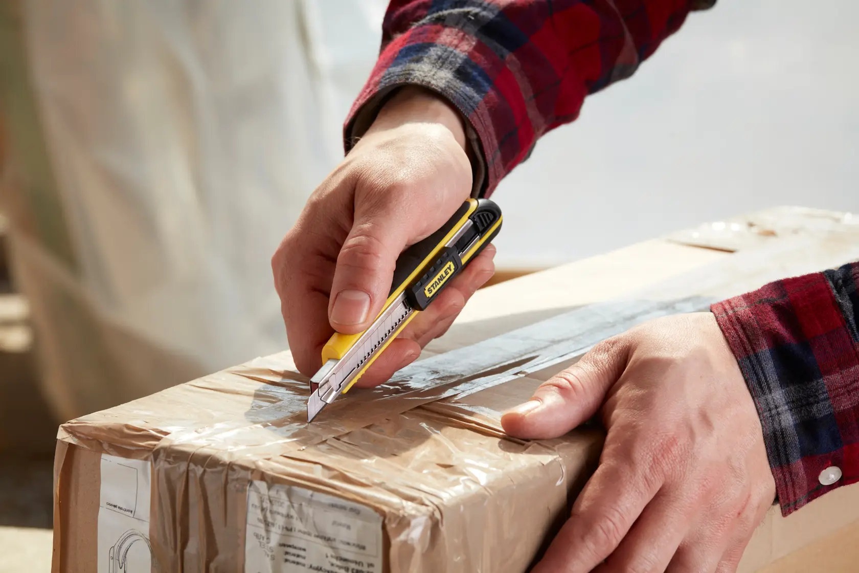 Photo of hands using STANLEY 0-10-475 utility knife to cut open a taped cardboard box.