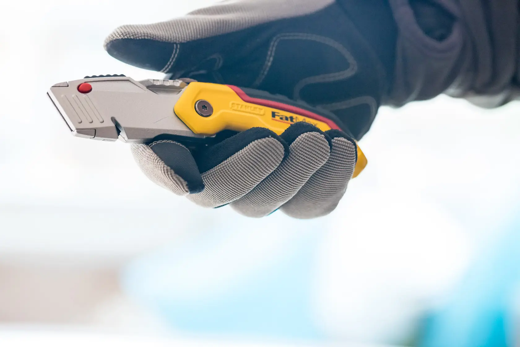 STANLEY 0-10-825 utility knife held in a gloved hand, close-up, yellow and silver handle visible.