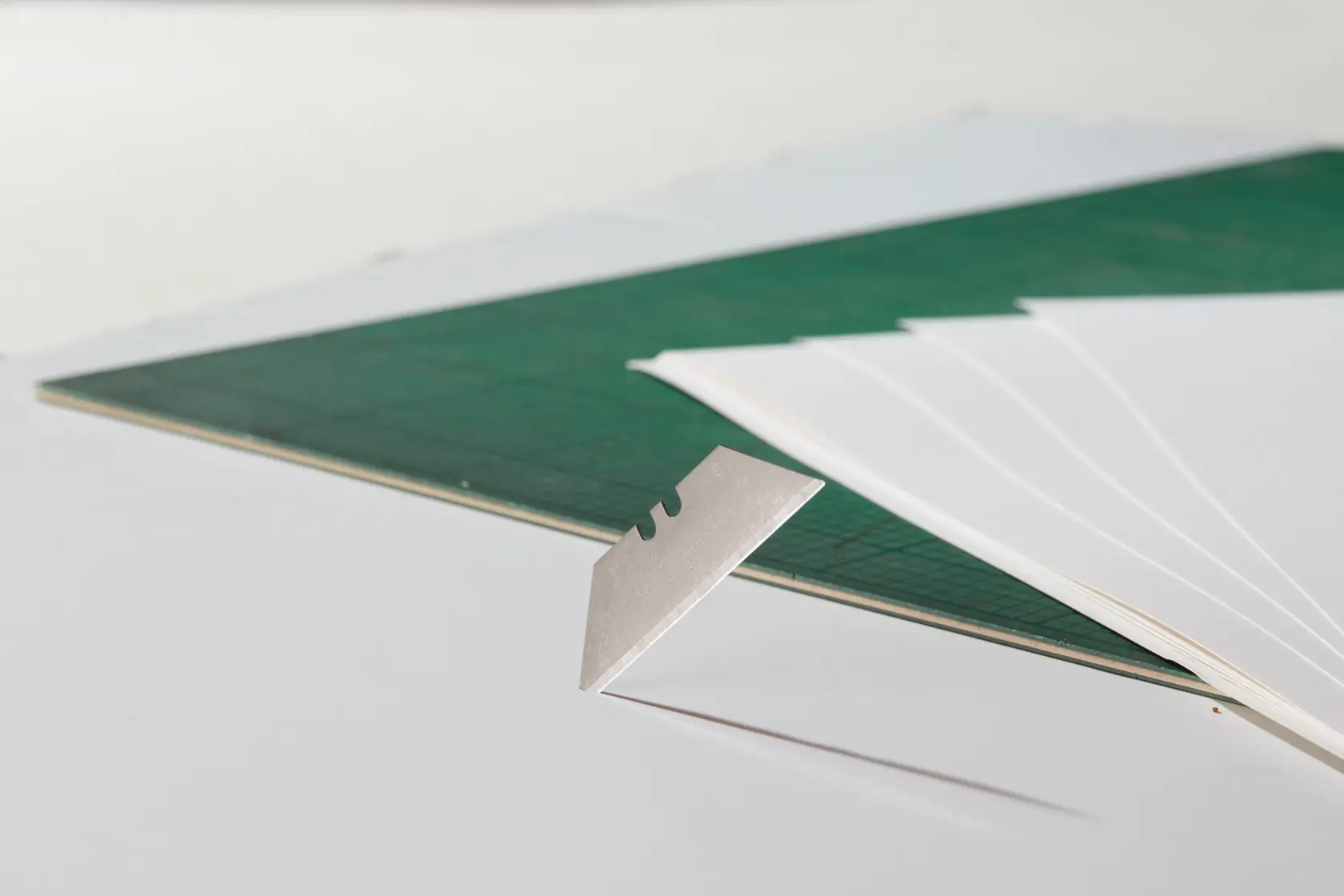 STANLEY 0-11-700 utility blade close-up with green cutting mat and white sheets in background.
