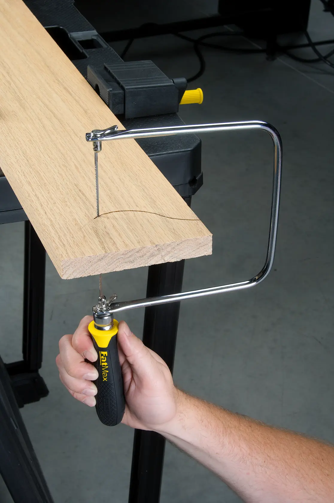 Photo of STANLEY 0-15-106 coping saw in use cutting a curved line in a wooden board from side angle.