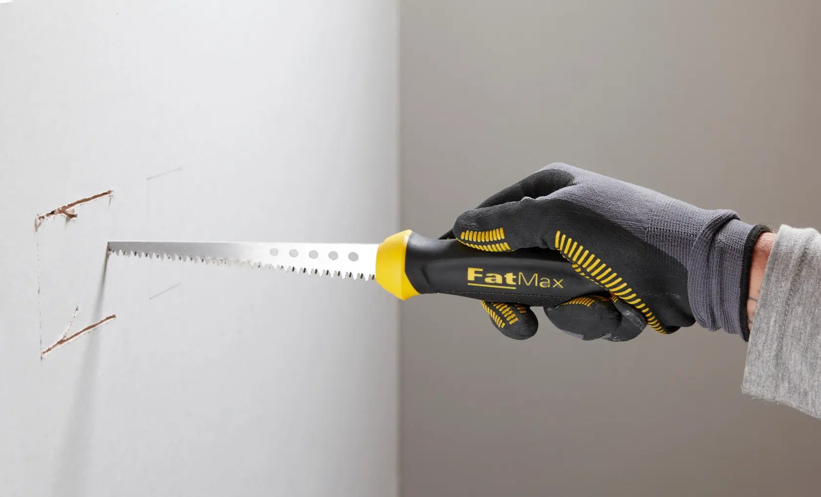STANLEY 0-20-556 hand saw with black and yellow FatMax handle cutting drywall, close-up photography.