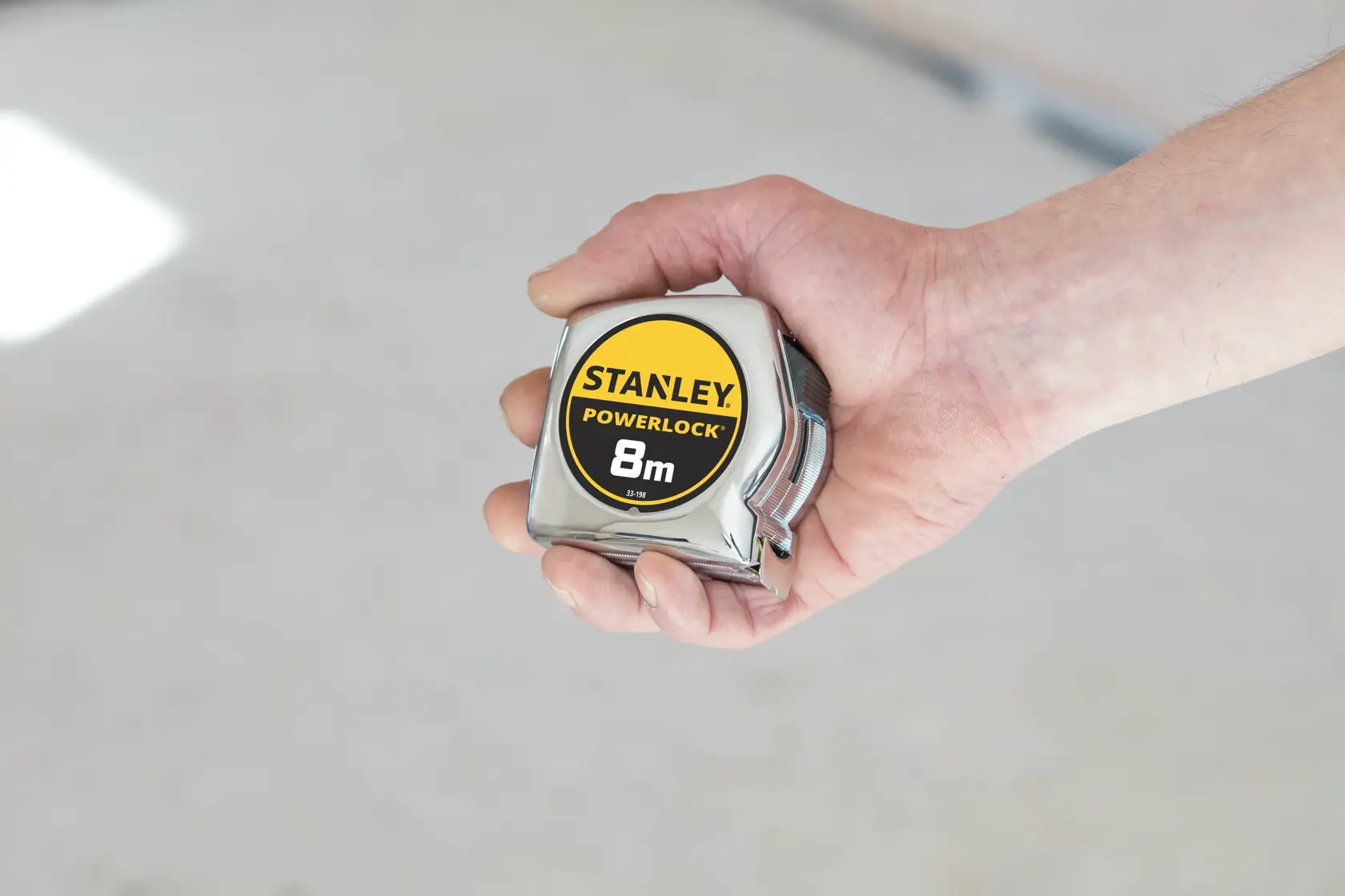 Stanley 0-33-198 Powerlock 8m Maßband in der Hand gehalten, Chrom-Finish, Produktfotografie.