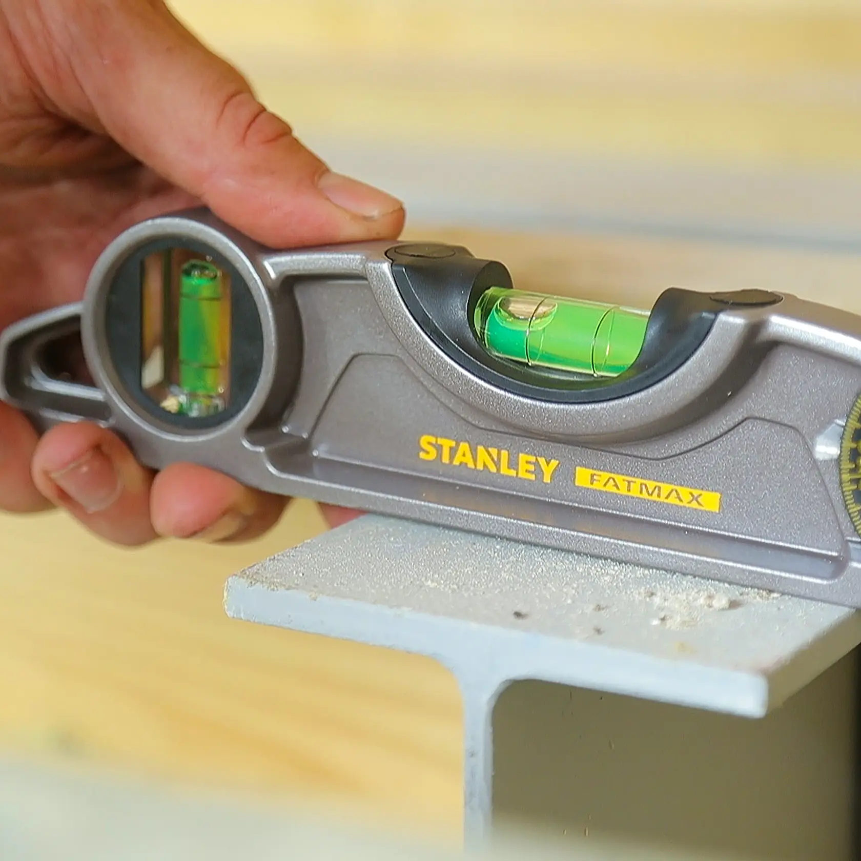 Photo of STANLEY 0-43-609 FATMAX spirit level in use, silver body, visible bubble vials, held by hand.