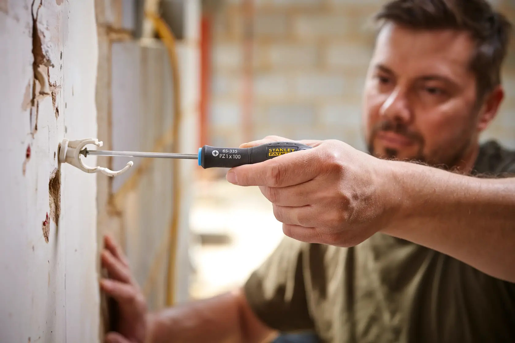 Stanley 0-65-335 screwdriver in use, close-up of hand installing wall bracket, construction setting.
