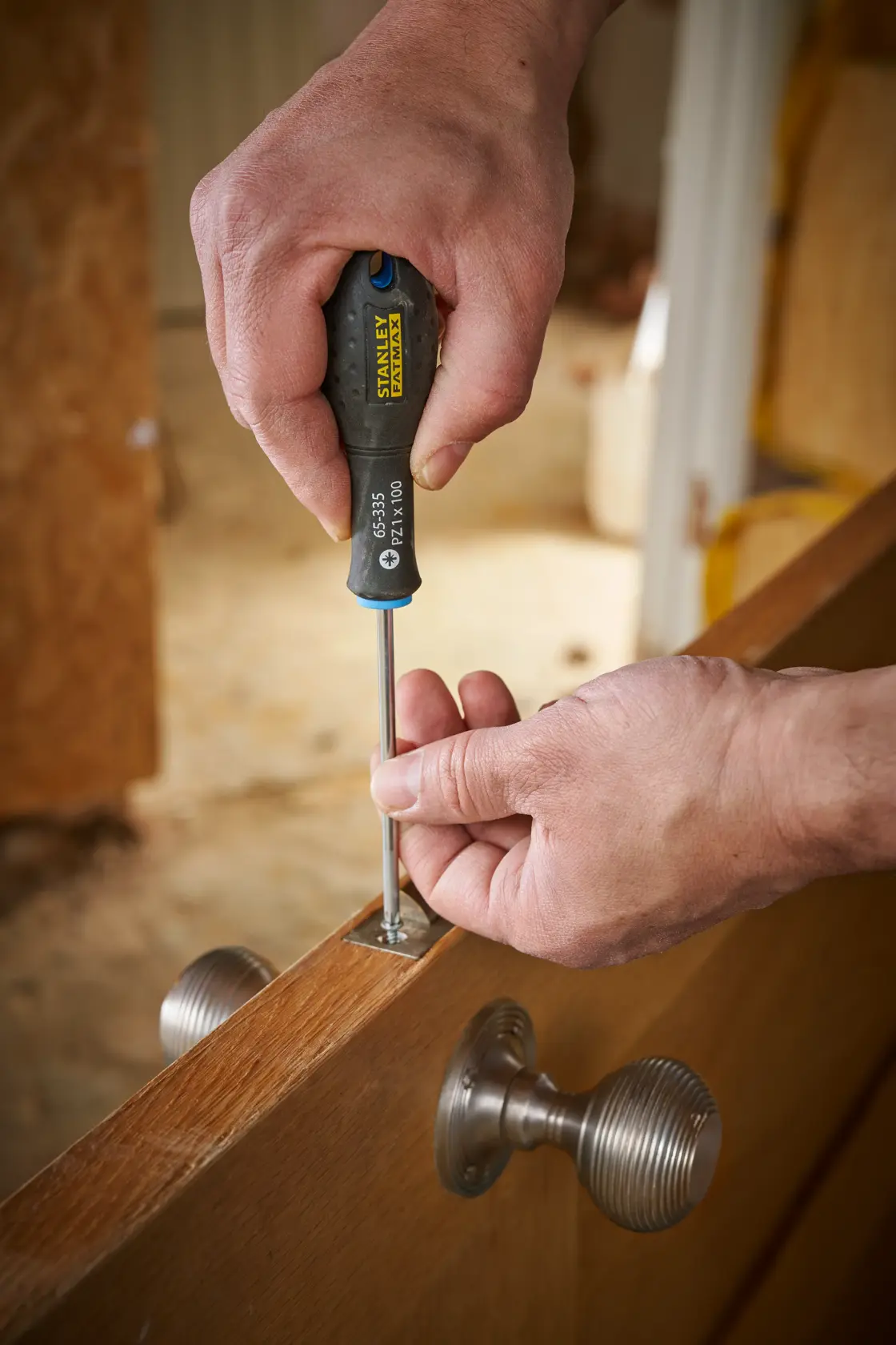 Photo of STANLEY 0-65-335 screwdriver used to tighten screw on metal hinge in wooden door.