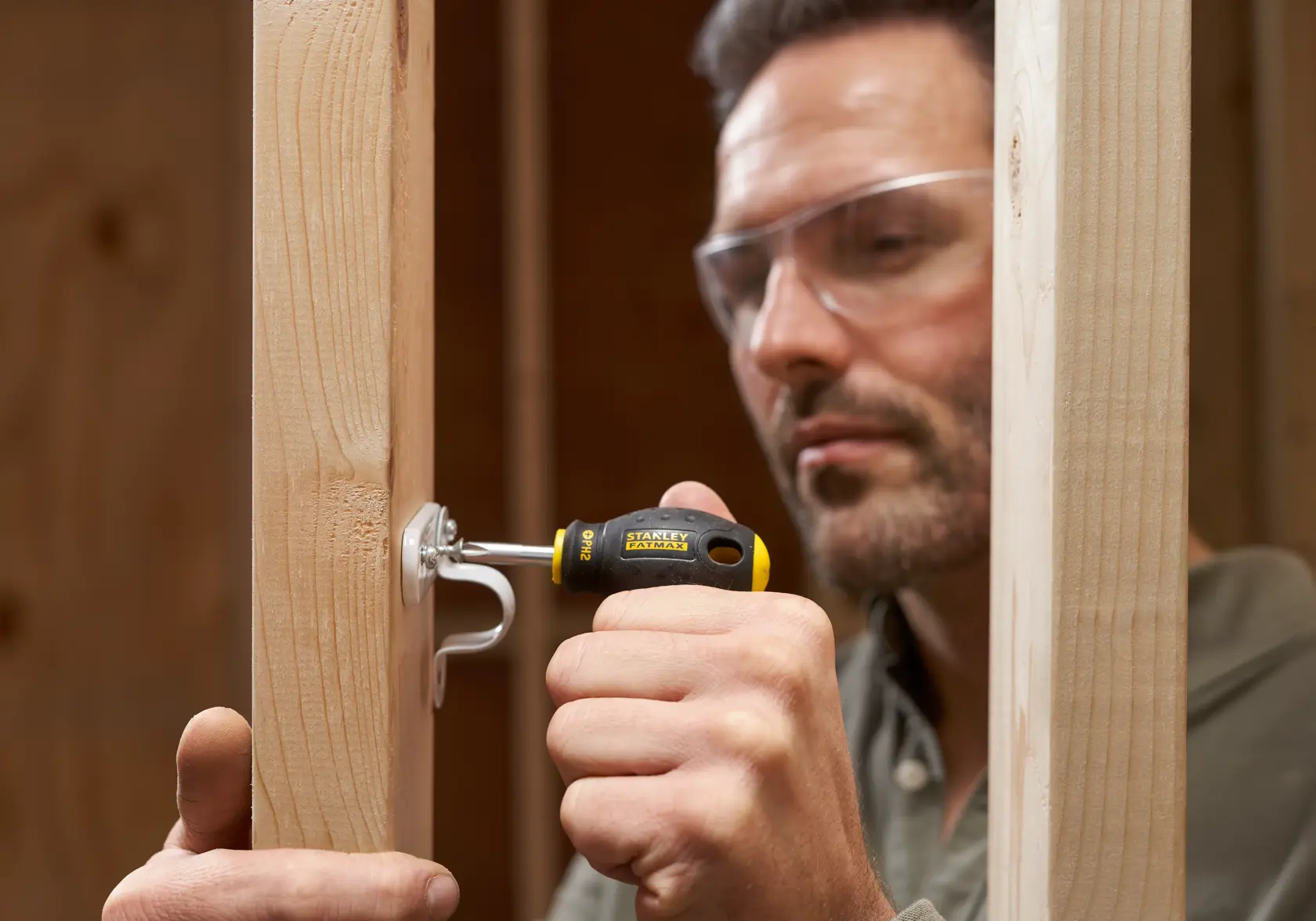 STANLEY 0-65-407 screwdriver used to fasten hook to wooden stud, shown in construction setting.