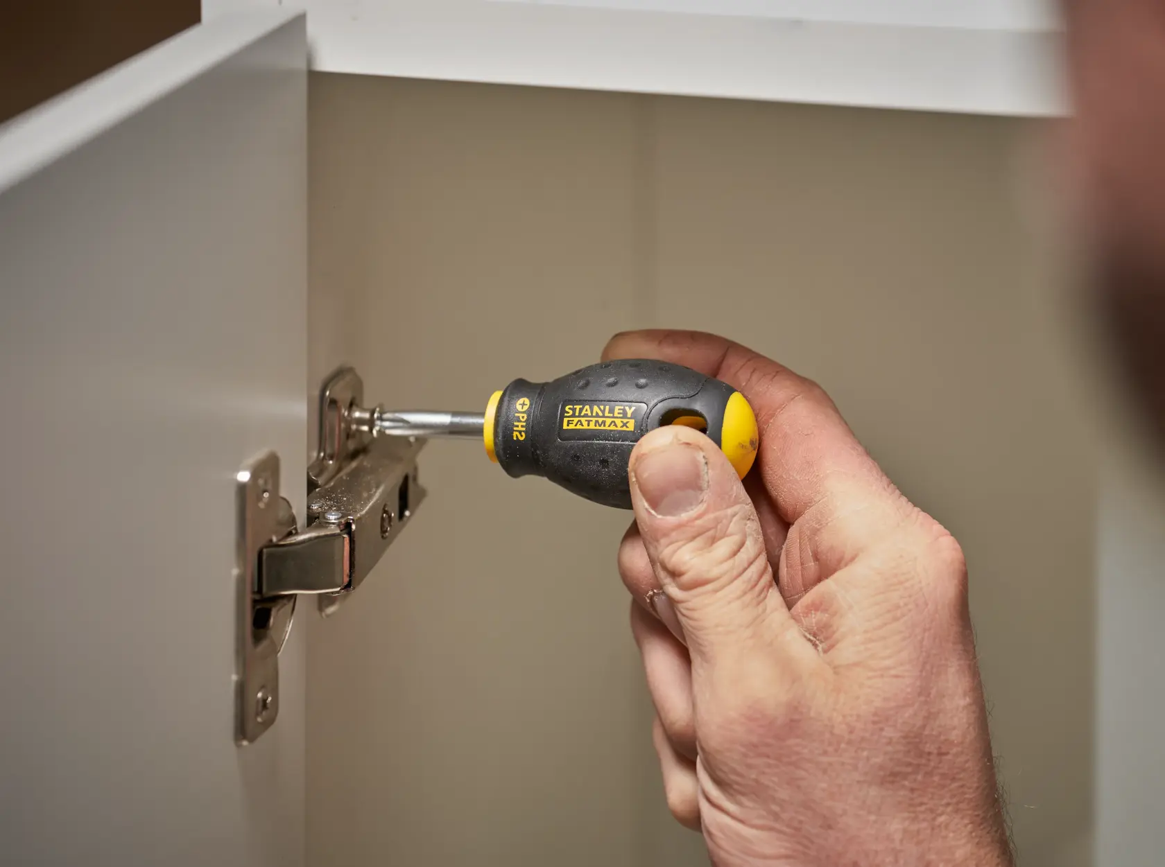 STANLEY 0-65-407 stubby screwdriver with black and yellow handle in use tightening a cabinet hinge.