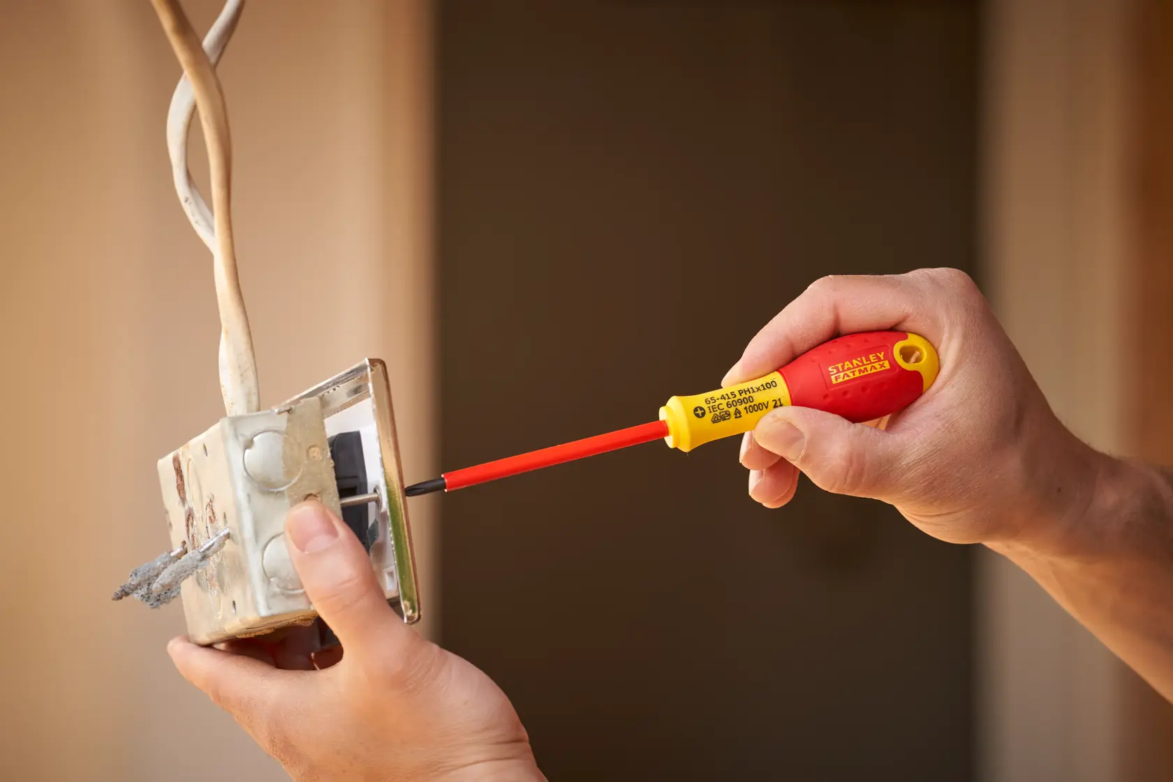 STANLEY 0-65-415 insulated screwdriver with red and yellow handle used for electrical work on a wall switch.