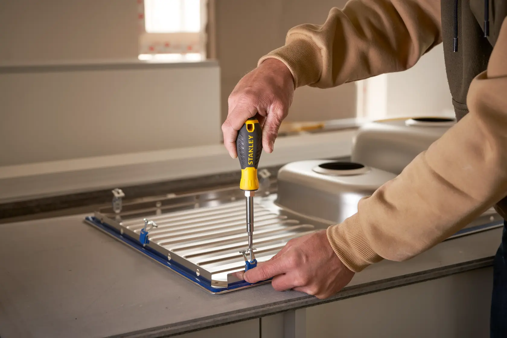 STANLEY 0-68-012 screwdriver used to install a metal sink in a kitchen, close-up from side.