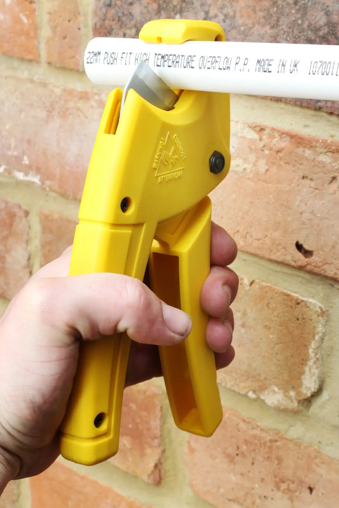 STANLEY 0-70-450 gelber Kunststoffrohrschneider in der Hand, schneidet weißes Rohr, Nahaufnahme.