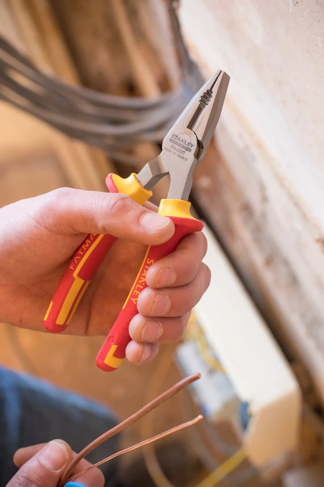 Photo of STANLEY 0-84-000 insulated combination pliers with red and yellow handles being used to cut copper wire.