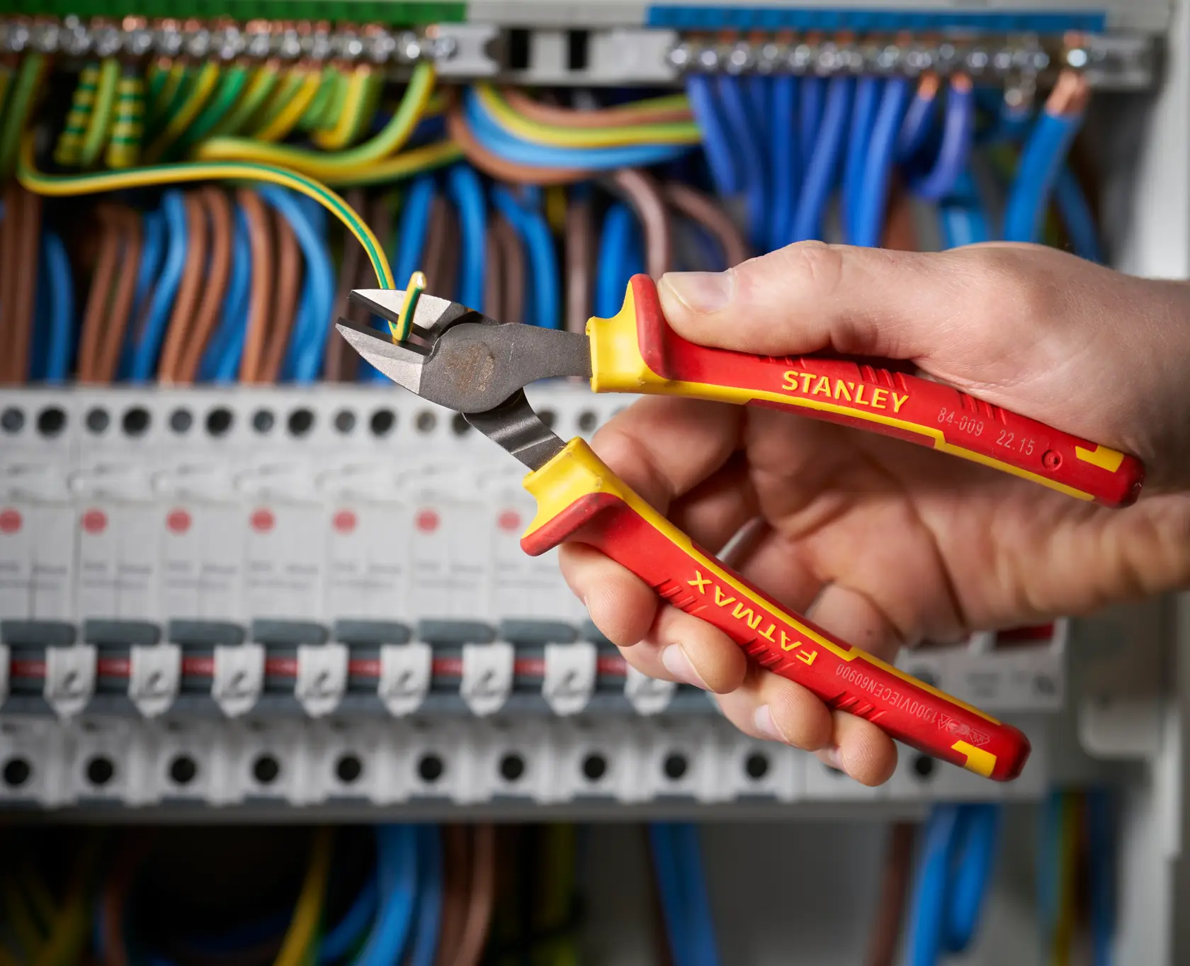 STANLEY 0-84-009 insulated diagonal cutting pliers held by hand, cutting wire in electrical panel.
