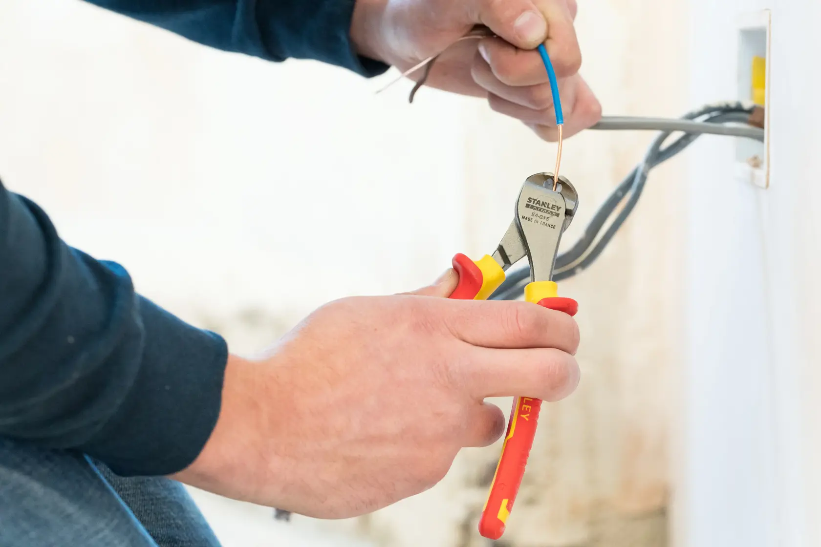 Photo of STANLEY 0-84-016 insulated pliers cutting electrical wire near outlet, close-up view.