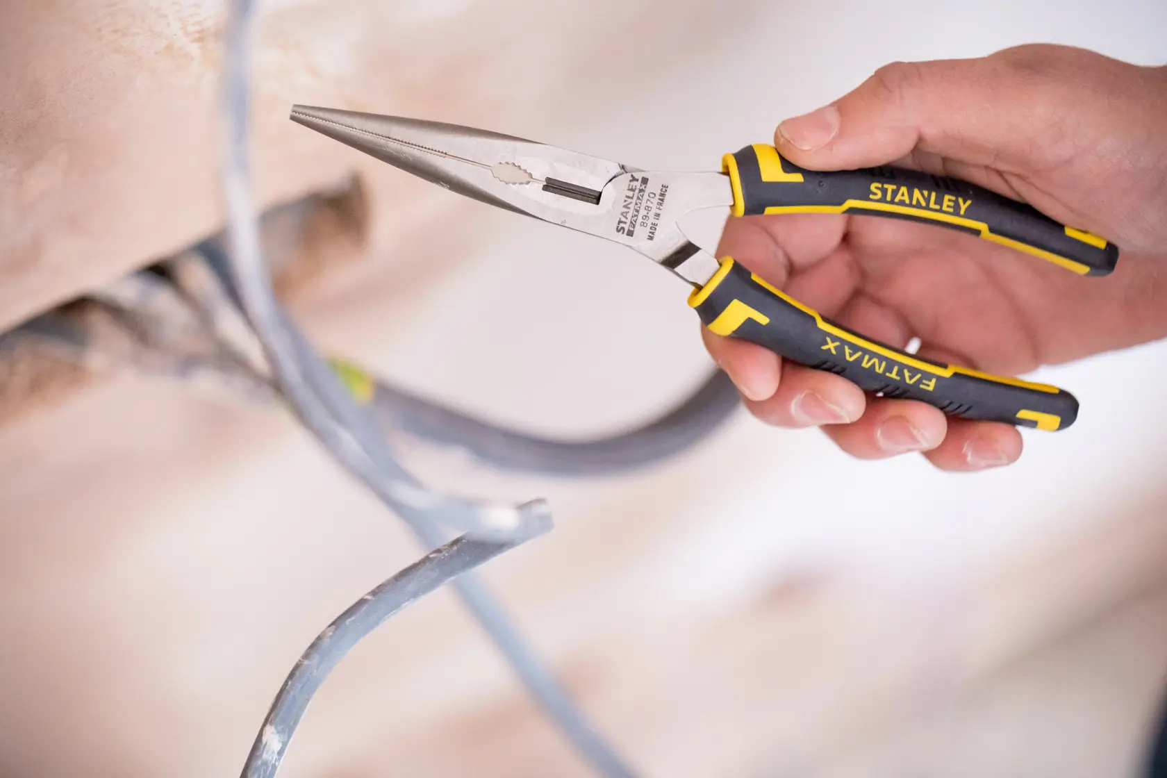 Stanley 0-89-870 FATMAX long nose pliers with black and yellow handles held, gripping electrical wire.