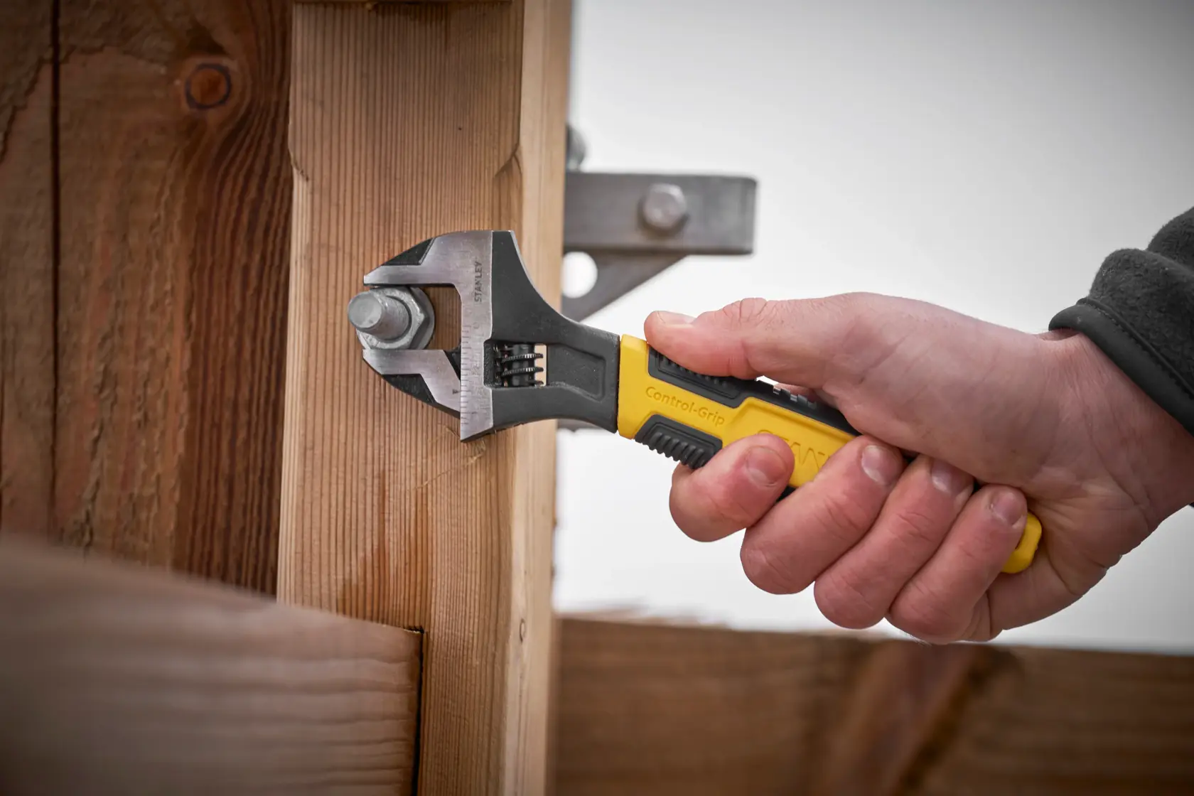 Stanley 0-90-949 verstellbarer Schraubenschlüssel mit gelbem Griff dreht Bolzen an Holzstruktur, Seitenansicht.