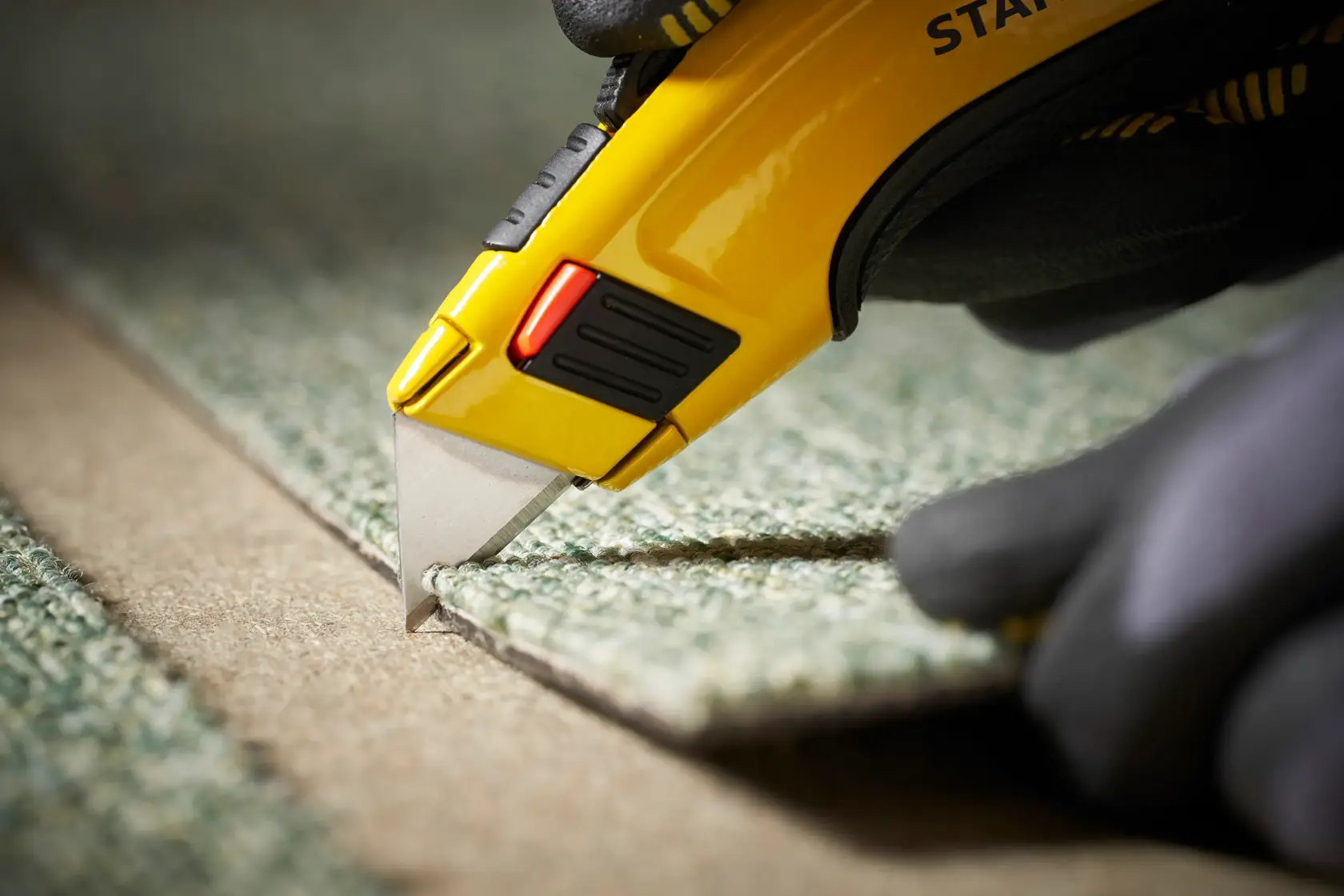 STANLEY 1-11-700 utility knife cutting carpet, close-up photography highlighting yellow handle and blade.