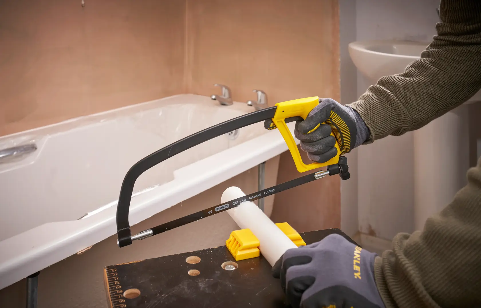 STANLEY 1-15-122 Bügelsäge schneidet weißes PVC-Rohr im Badezimmer, Nahaufnahme Aktion.