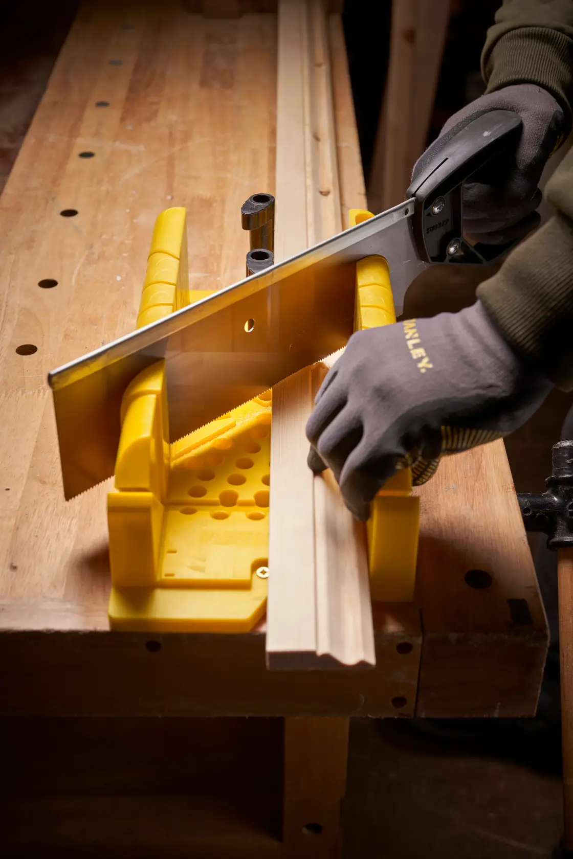 STANLEY 1-20-600 photography of yellow mitre box and saw cutting wood trim on workbench, angled view.