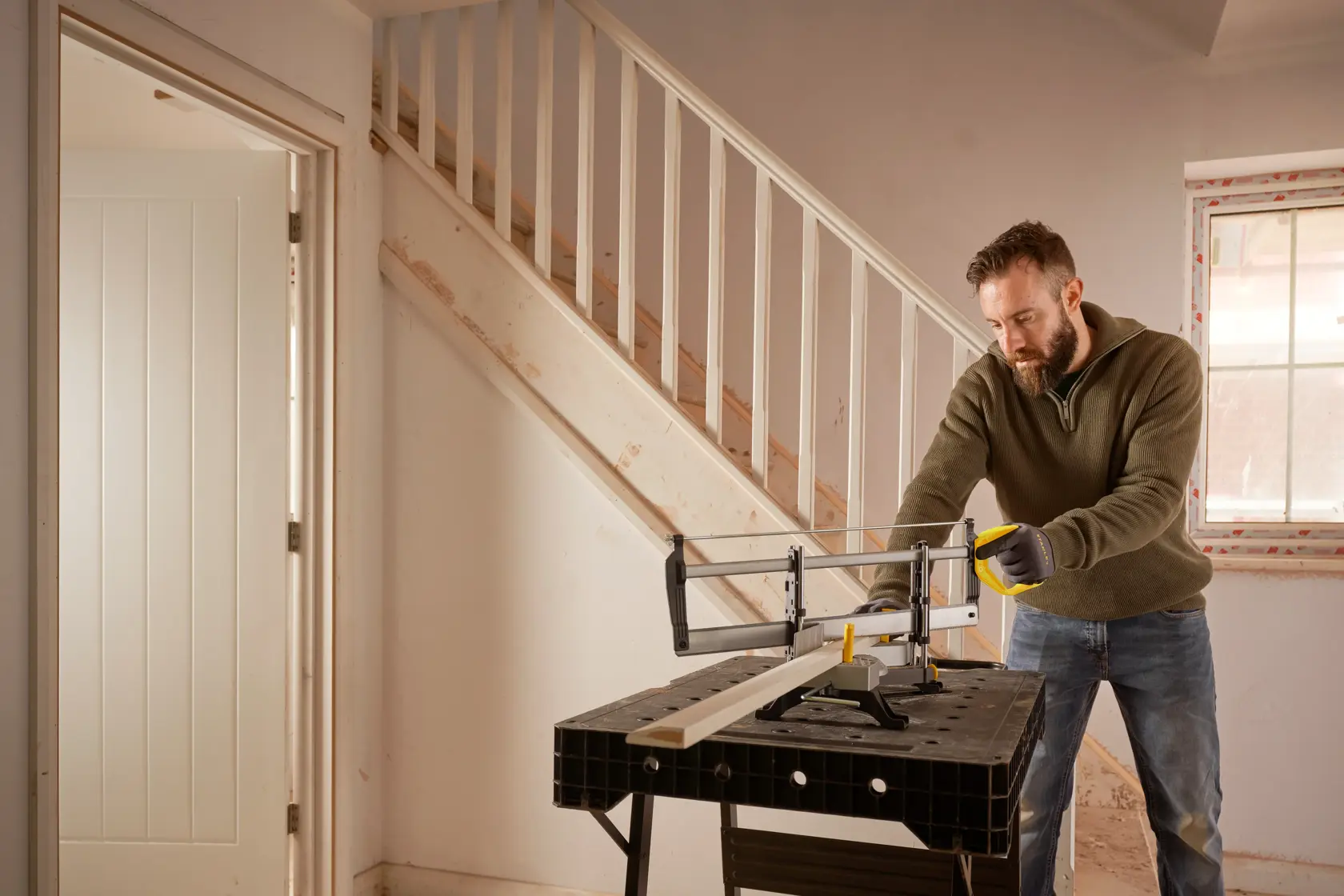 STANLEY 1-20-800 Handsäge wird auf einer Werkbank im Innenbereich von einer Person genutzt, um Holz nahe einer Treppe zu sägen.