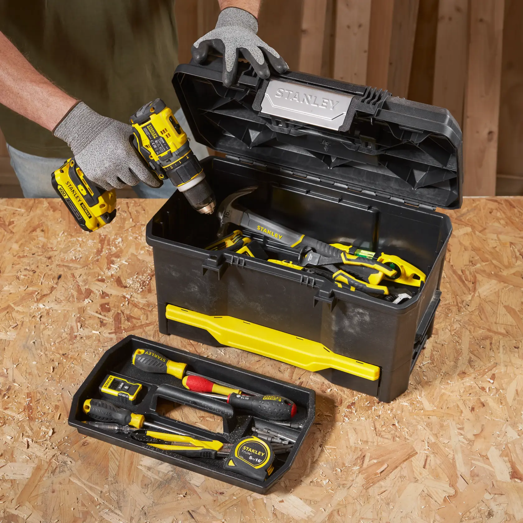 STANLEY 1-70-316 black and yellow toolbox with assorted hand tools and open lid, photo shows person holding drill.