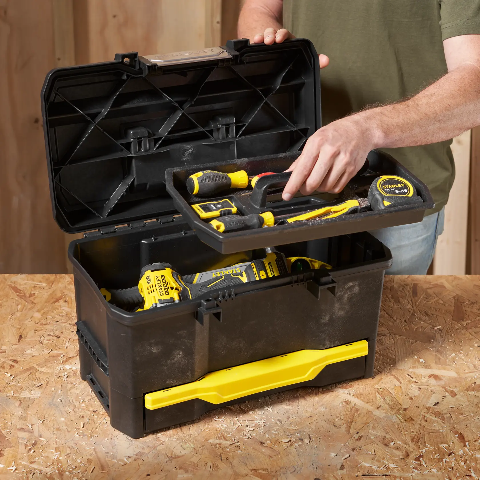 Photo of STANLEY 1-70-316 black and yellow toolbox with tools on a workbench, lid open, person accessing tray.
