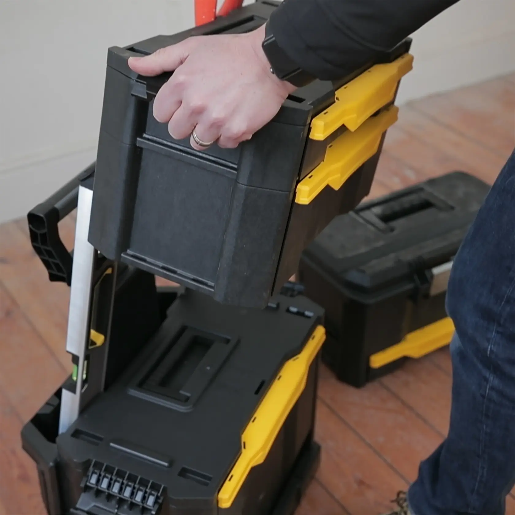 STANLEY 1-79-206 stapelbarer Werkzeugkasten in Schwarz und Gelb wird von Hand gehoben, Nahaufnahme Fotografie.