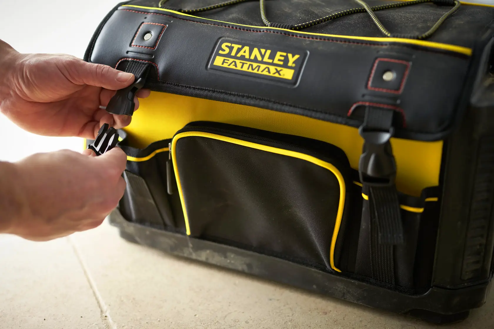 STANLEY 1-79-213 tool bag, black and yellow, front angle, hands fastening side buckle.