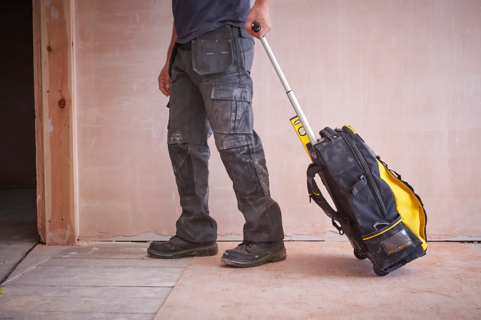 STANLEY 1-79-215 rolling tool bag with yellow and black design, extended handle, shown in use on worksite floor.
