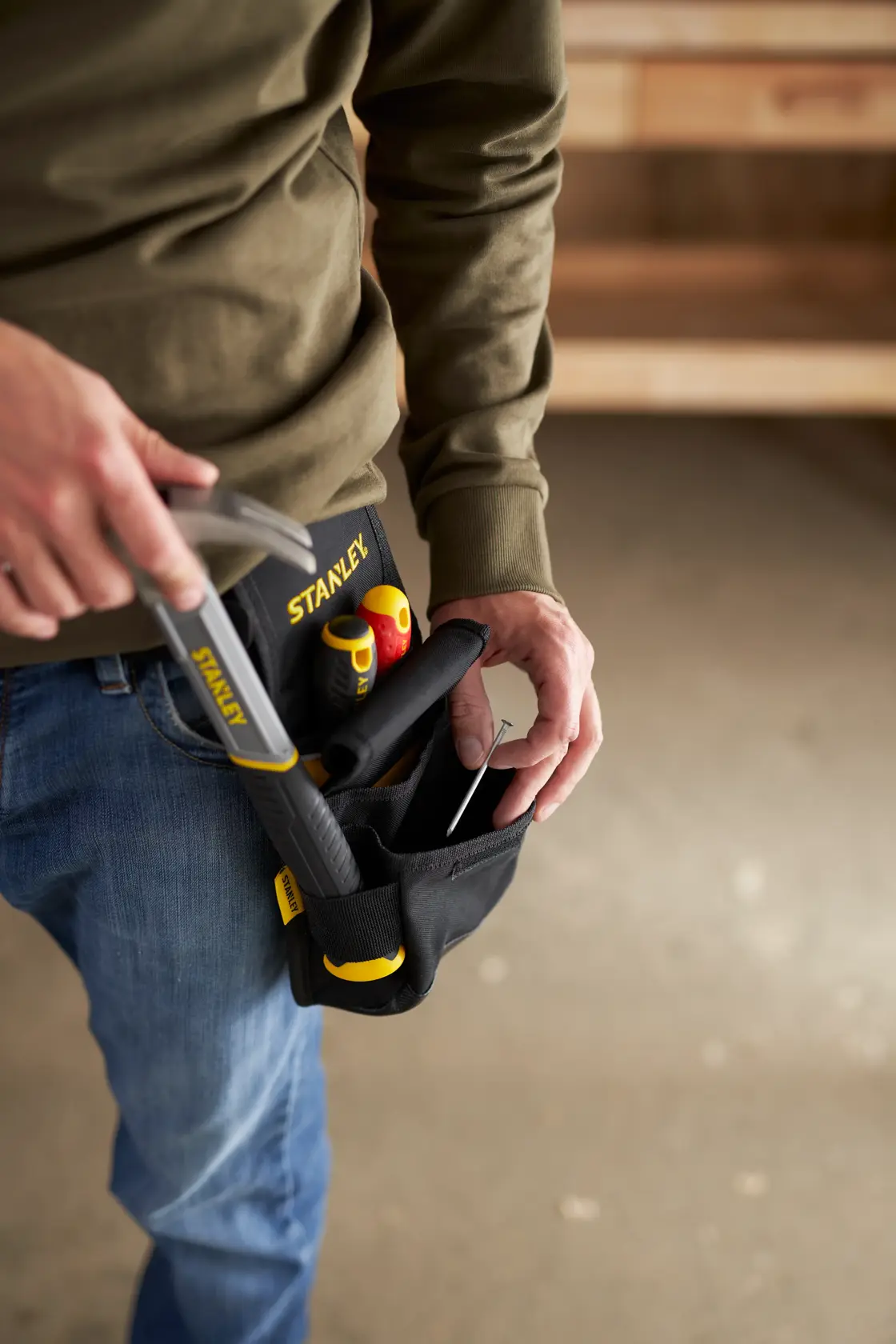 Foto einer Person mit STANLEY Werkzeuggürteltasche SKU 1-93-329 und Handwerkzeugen in einer Werkstatt.