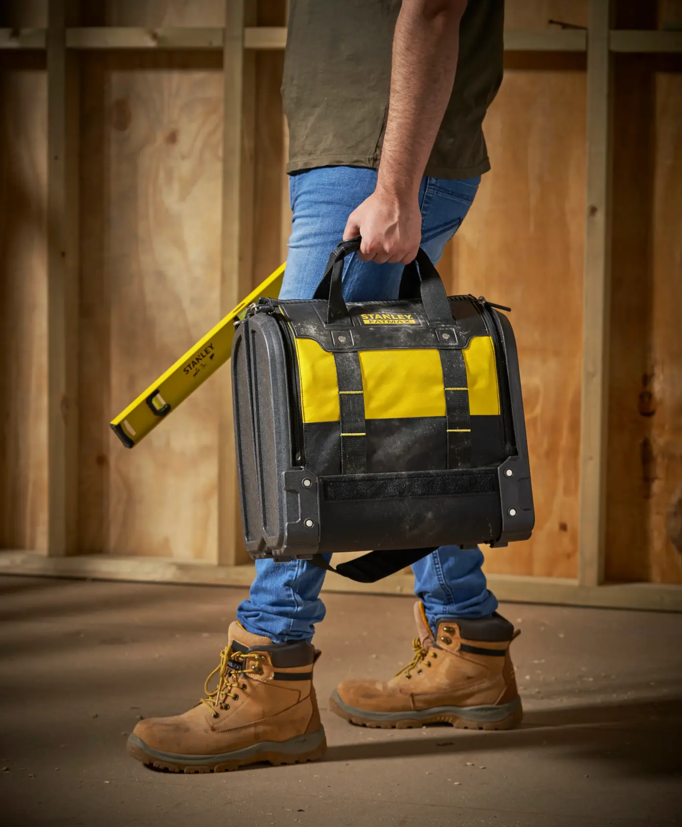 STANLEY 1-94-231 tool bag with yellow and black colors, carried by person on worksite, side view.