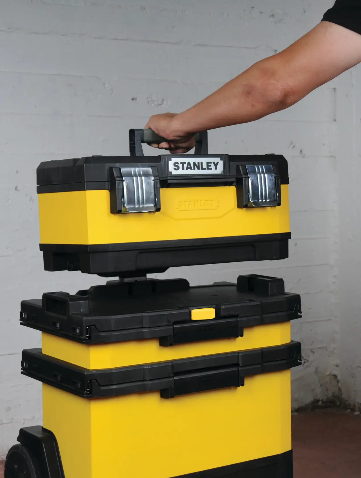 STANLEY 1-95-621 yellow and black stackable toolboxes, with top box being lifted by a hand, side view.
