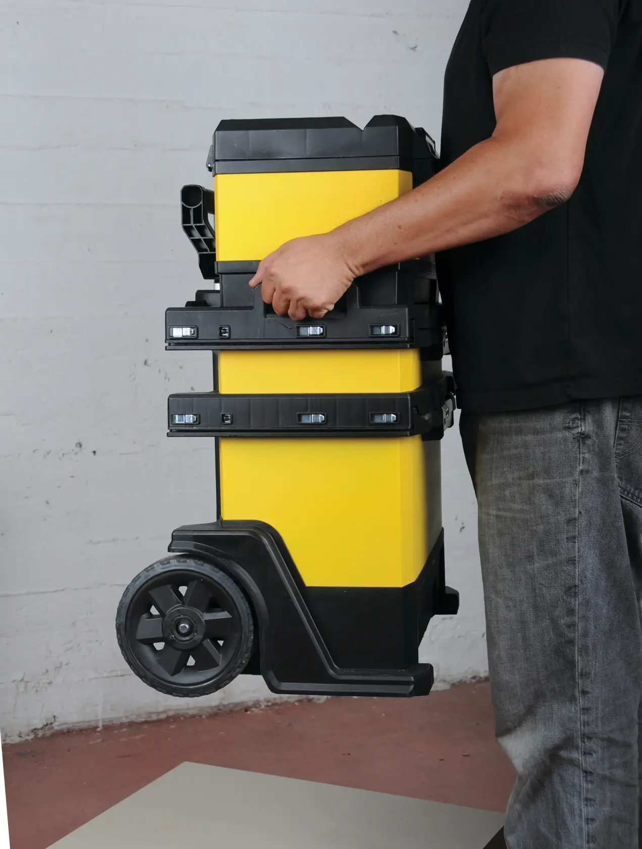 STANLEY 1-95-621 mobile tool chest in yellow and black, carried by a person, side view.