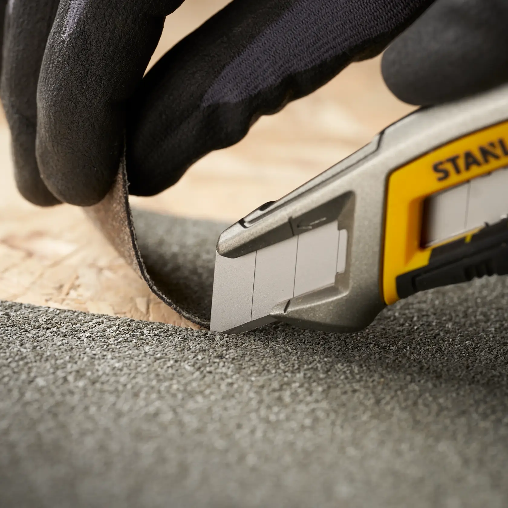 STANLEY 2-11-718 utility knife cutting roofing material, close-up with gloved hand, product photography.