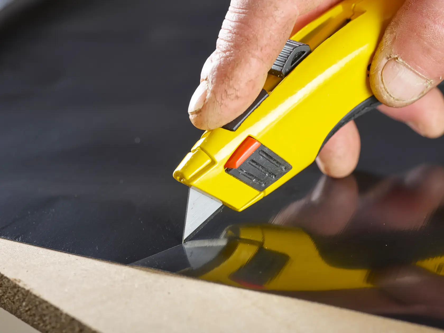 STANLEY 2-11-921 Universalmesser mit gelbem Griff schneidet schwarze Platte, Nahaufnahme, Produkt im Einsatz.