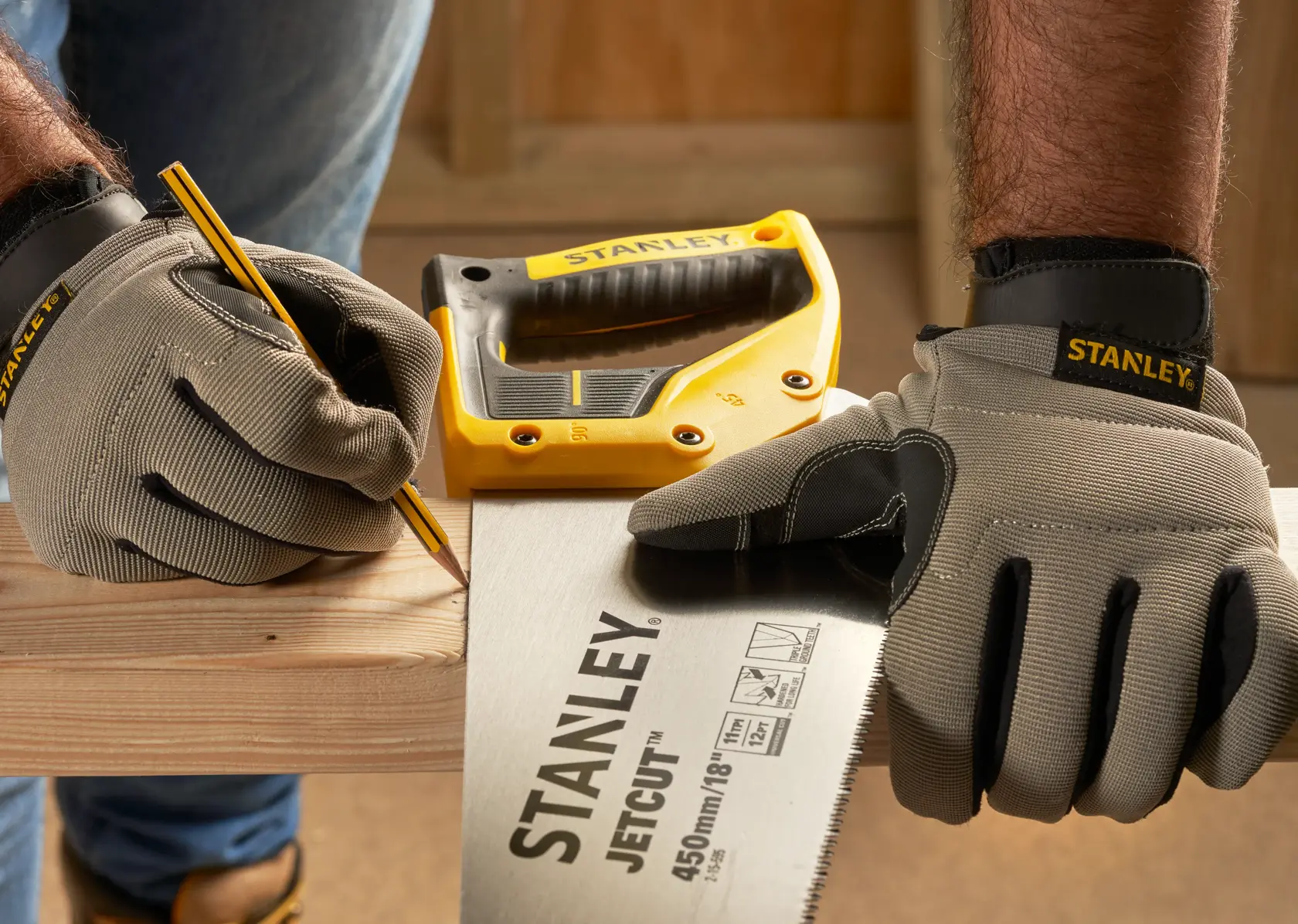 Foto von STANLEY 2-15-595 Handsäge und Handschuhen auf Holz, mit Bleistift und gelbem STANLEY Werkzeug im Hintergrund.