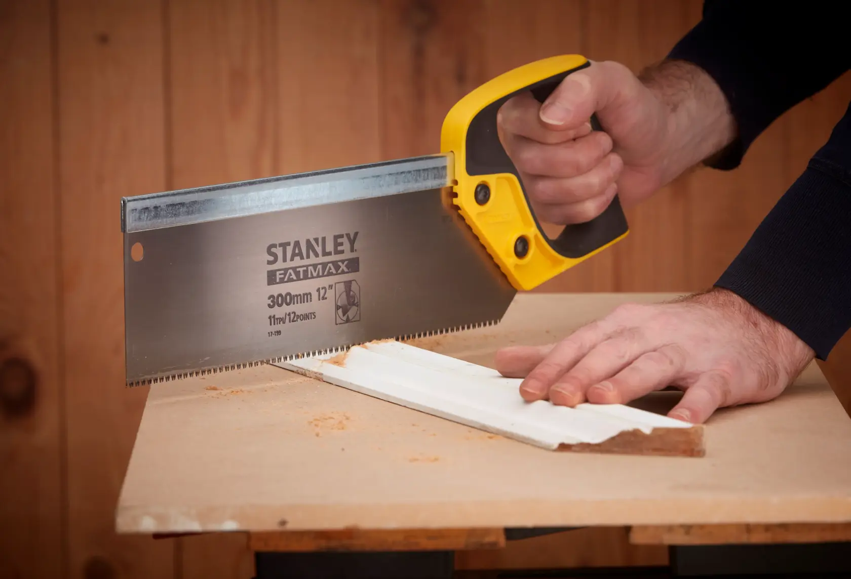 Stanley 2-17-199 hand saw with yellow handle cutting white molding on workbench, side angle.