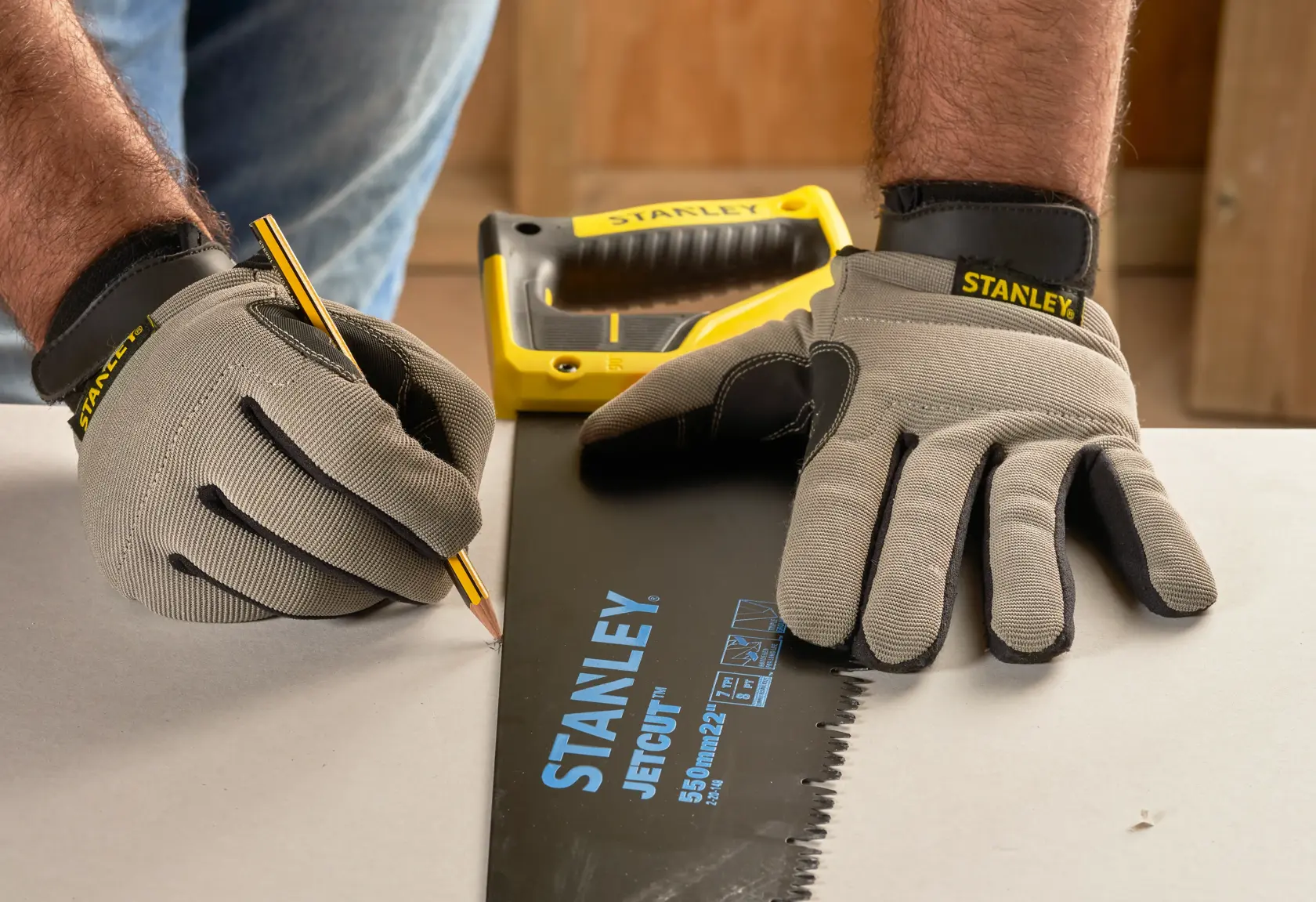 Foto der STANLEY 2-20-149 Handsäge zum Markieren mit Handschuhen und Bleistift auf einer Arbeitsfläche.
