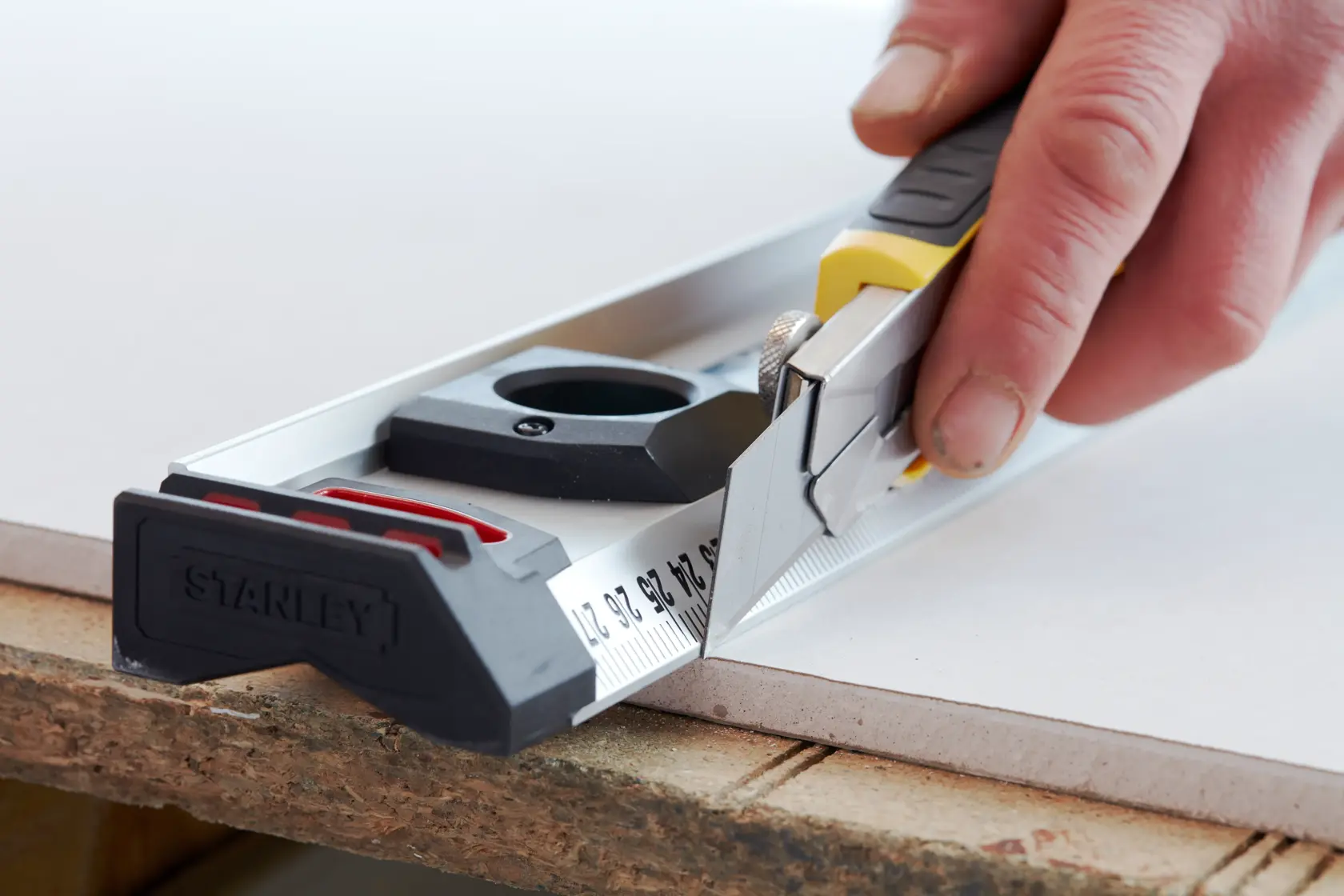 STANLEY 3-11-725 utility knife with ruler guide cutting sheet material, close-up photography.