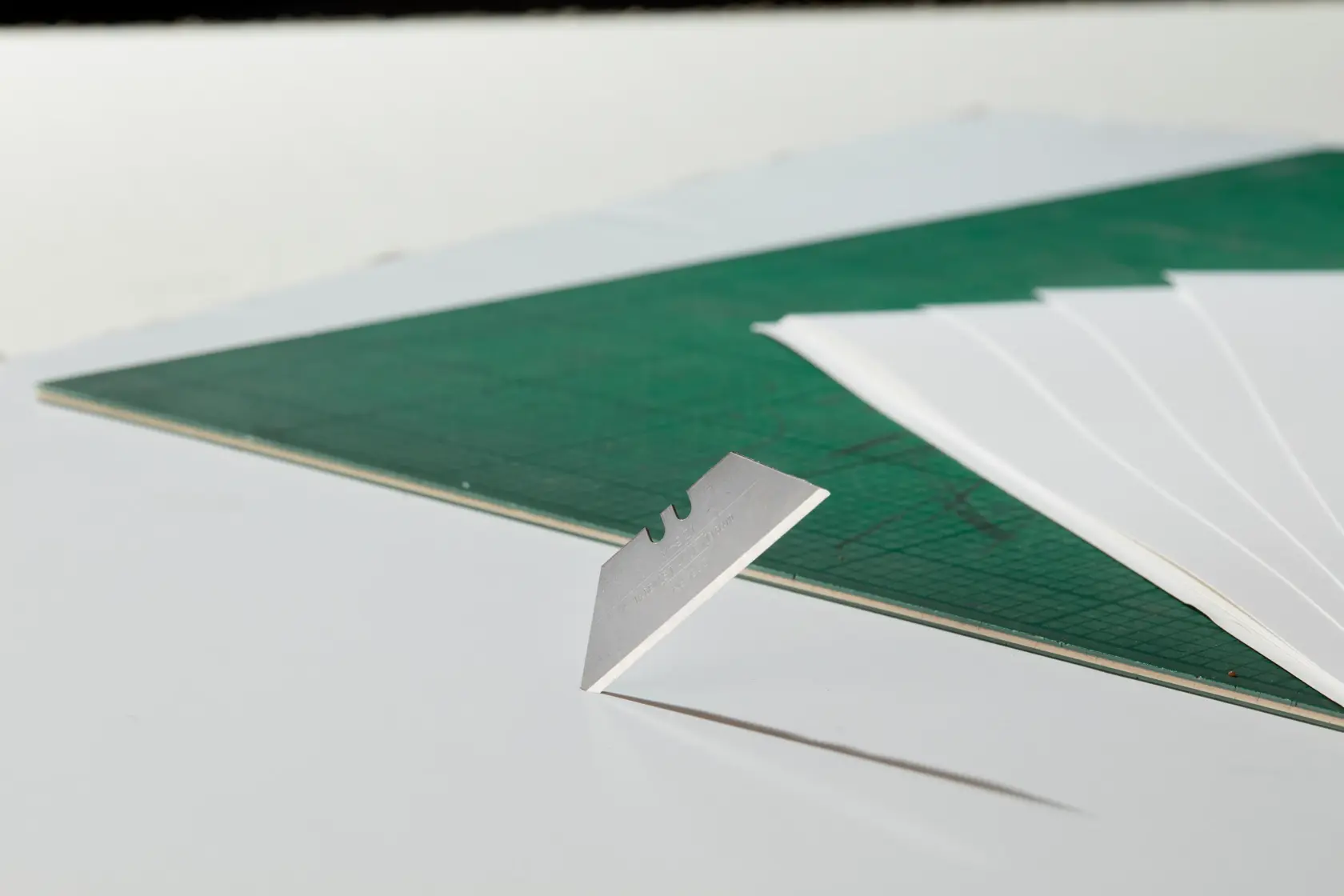 STANLEY 4-11-921 utility blade on white table with green cutting mat and white sheets, side angle.