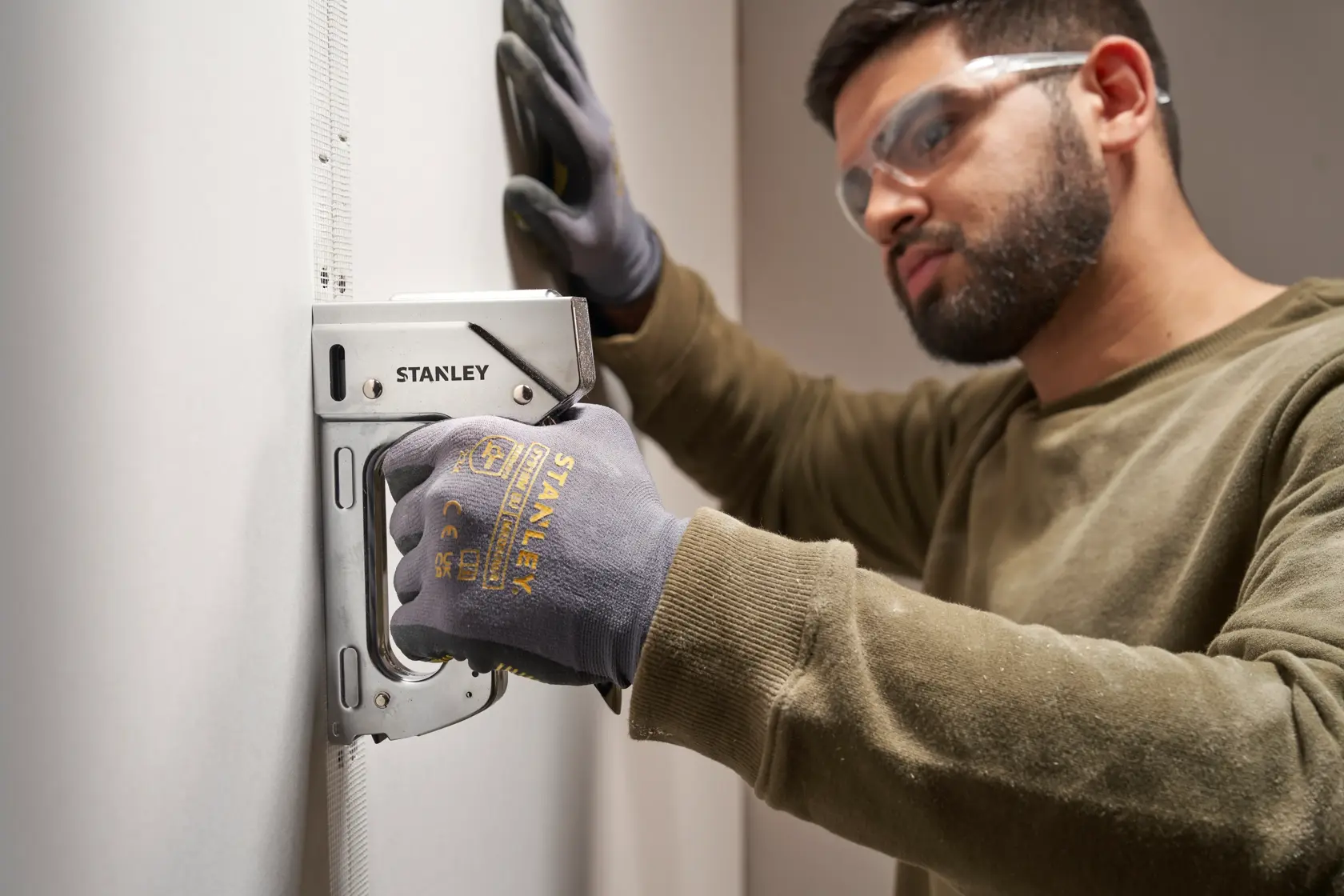 Photo of STANLEY 6-TR110 stapler used on wall by person wearing STANLEY gloves.