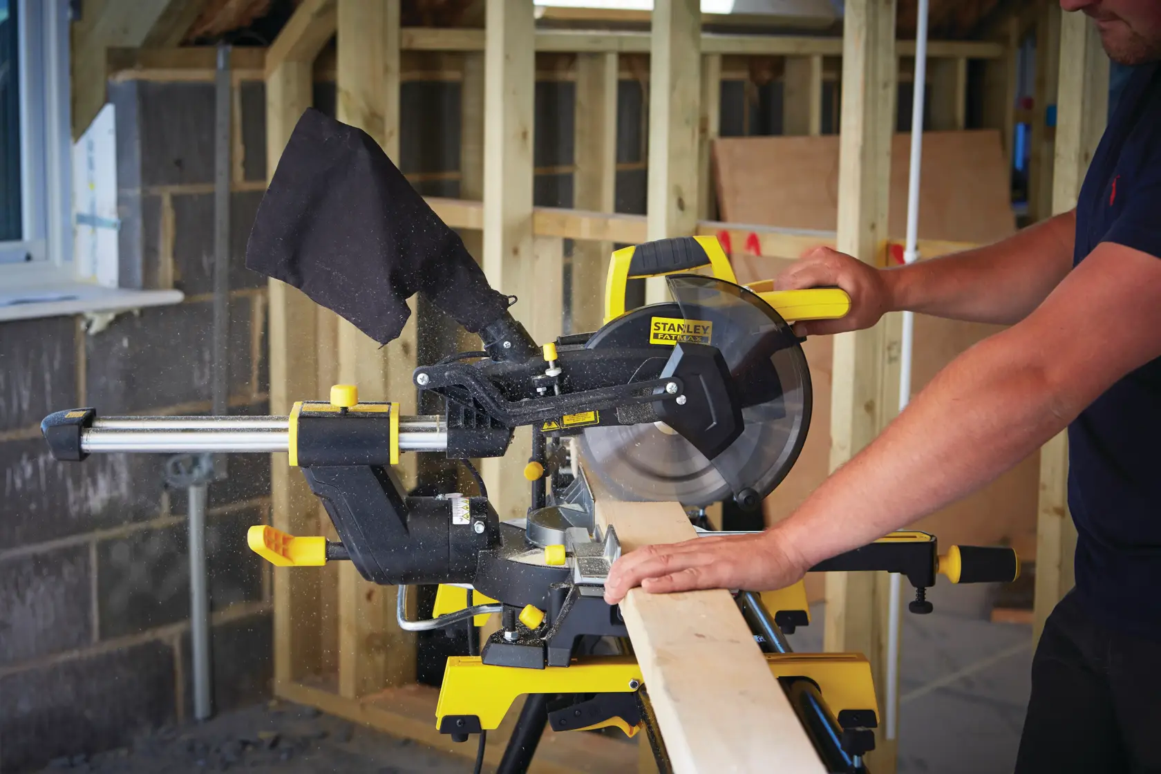 Photo of STANLEY FME721-QS sliding mitre saw in use, cutting a wooden board in a construction setting.