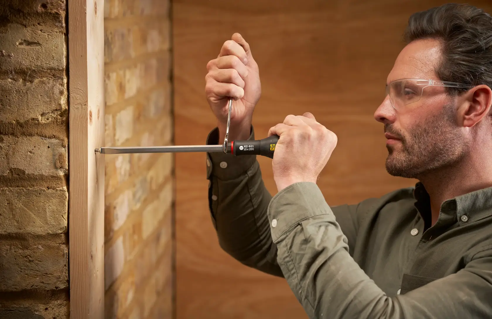Photo of STANLEY FMHT0-62621 screwdriver used to fasten screw in wooden frame against brick wall.