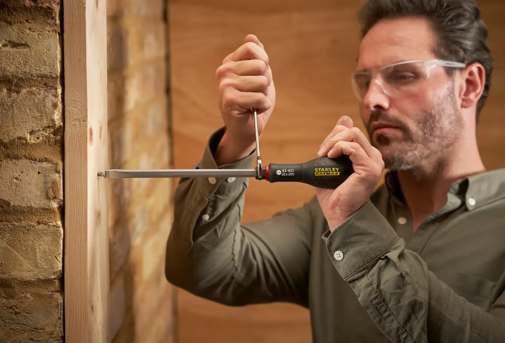 STANLEY FMHT0-62621 screwdriver used to drive a screw into wood, close-up showing tool in hand.