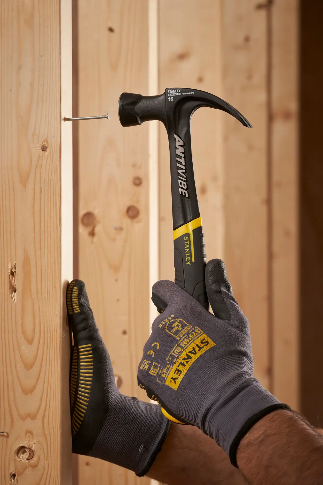 Photo of STANLEY FMHT1-51275 claw hammer with black and yellow handle driving nail into wooden beam.