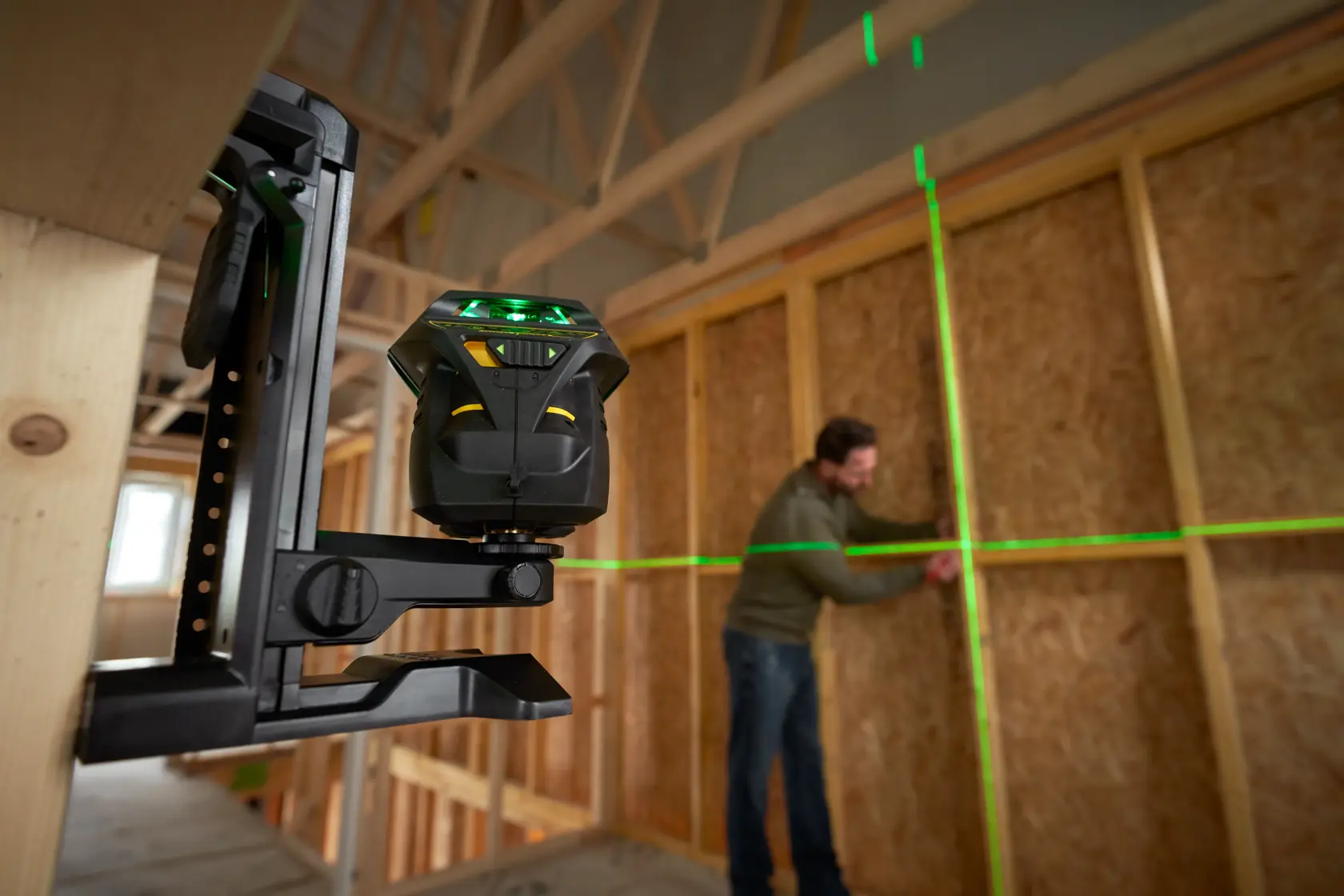 STANLEY FMHT1-77356 laser level projecting green lines on wall in construction site, side angle view.