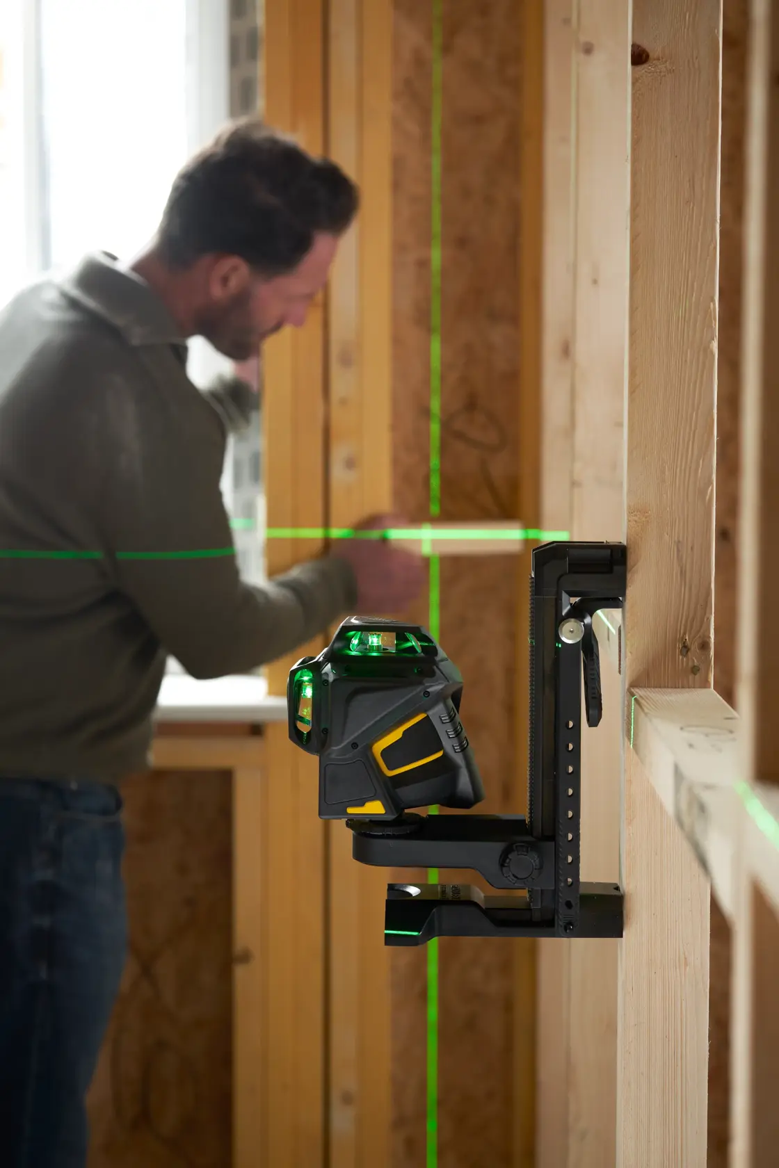 STANLEY FMHT1-77356 green beam laser level mounted on wall in construction setting, man working in background.